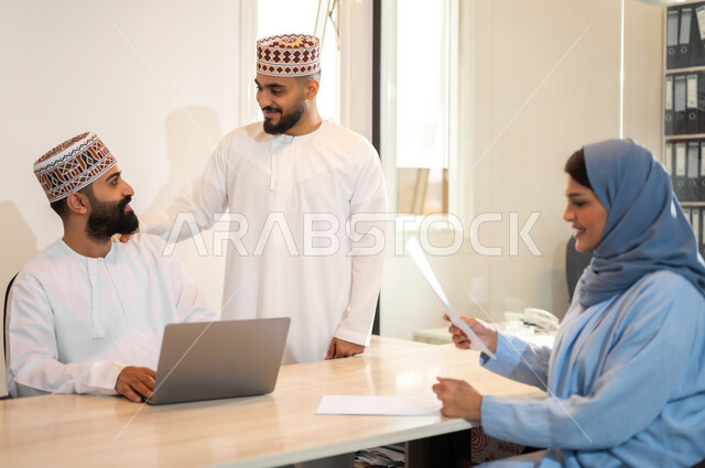 Comfortable environment in Omani companies, exchanging conversations and views between colleagues, administrative professions and jobs in the Sultanate of Oman, gestures of joy and happiness, the concept of employee training and development, an Arab Gulf Omani work team holding a meeting inside an office, using modern technical devices to accomplish tasks