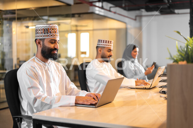 مفهوم تدريب وتطوير الموظفين, فريق عمل عربي خليجي عماني يجلسون داخل مكتب، إيماءات البهجة والسرور، بيئة مريحة في الشركات العمانية، استخدام الأجهزة التقنية الحديثة في إنجاز المهام، مهن ووظائف إدارية في سلطنة عمان، تبادل الأحاديث ووجهات النظر بين الزملاء