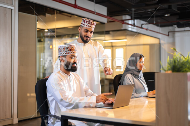 إيماءات البهجة والسرور، مفهوم تدريب وتطوير الموظفين, فريق عمل عربي خليجي عماني يجلسون داخل مكتب، بيئة مريحة في الشركات العمانية، استخدام الأجهزة التقنية الحديثة في إنجاز المهام، مهن ووظائف إدارية في سلطنة عمان، تبادل الأحاديث ووجهات النظر بين الزملاء