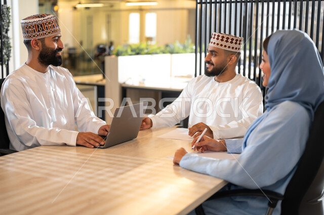 إيماءات البهجة والسرور، مفهوم تدريب وتطوير الموظفين, فريق عمل عربي خليجي عماني يجلسون داخل مكتب، بيئة مريحة في الشركات العمانية، استخدام الأجهزة التقنية الحديثة في إنجاز المهام، مهن ووظائف إدارية في سلطنة عمان، تبادل الأحاديث ووجهات النظر بين الزملاء