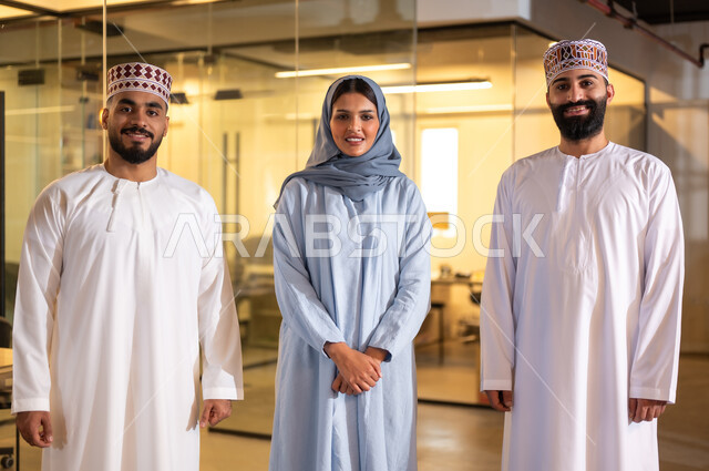 Administrative jobs and professions in the Sultanate of Oman, standing straight and looking at the camera with gestures of joy and pleasure, comfortable environment in Omani companies, an Arab Gulf Omani work team in a meeting inside an office, gestures of joy and pleasure