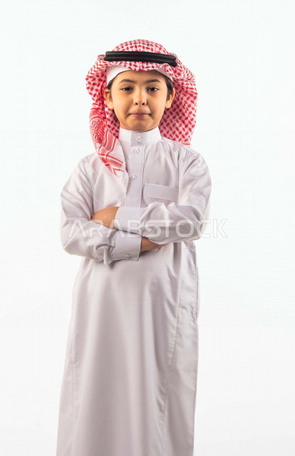 خلفية بيضاء لصبي صغير سعودي خليجي مبتسم وجميل ، ينظر الى الكاميرا بإيدي متقاطعة بإيماءات وجه ويدين مختلفة , بورتريه لطفل سعودي خليجي سعيد يرتدي الزي السعودي التقليدي مع شماغ وعقال , الاحتفال بعيد الفطر السعيد ،عيد الفطر المبارك