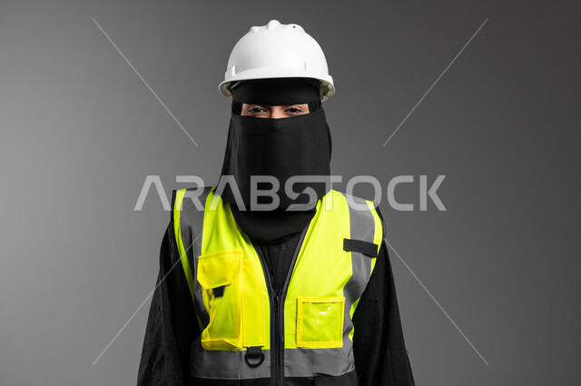 دور الهندسة الإنشائية في تطور المجتمع السعودي, مهن ووظائف نسائية في القطاع الهندسي, بورتريه مقرب لمهندسة عربية خليجية سعودية مسلمة منقبة ترتدي الخوذة البيضاء وسترة الحماية، الوقوف بظهر مشدود بإيماءات الثقة بالنفس، الإعمار بسواعد أبناء الوطن، خلفية رمادية