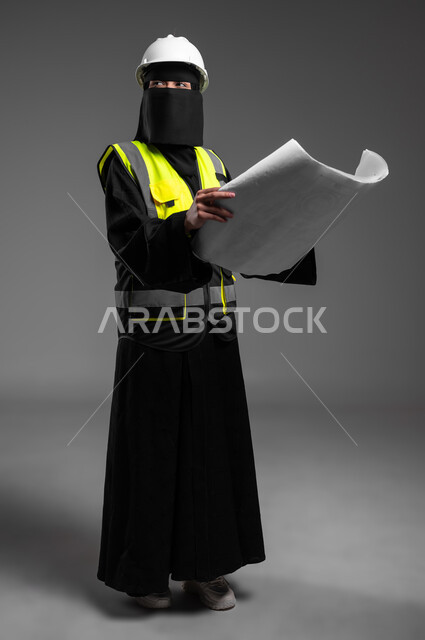 Architectural designs and blueprint auditing, the role of structural engineering in the development of Saudi society, women’s professions and jobs in the engineering sector, portrait of a veiled Saudi Gulf Arab Muslim engineer wearing a white helmet and protective vest holding the reconstruction plan, full-length body, gray background