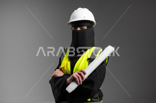 Standing and holding the architectural plan, the role of structural engineering in the development of Saudi society, women’s professions and jobs in the engineering sector, a close-up portrait of a veiled Saudi Gulf Arab Muslim engineer wearing a white helmet and protection vest, reconstruction with the arms of the nation’s sons, gray background