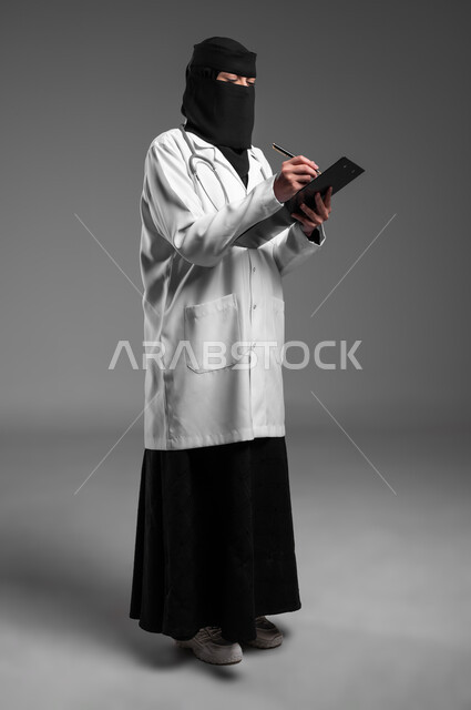 عمل النساء في مجال الرعاية الصحية, كتابة التقارير الطبية، تدوين وتسجيل الملاحظات حول حالة المريض،  بورتريه لطبيبة عربية خليجية سعودية مسلمة منقبة ترتدي المعطف الطبي وتضع سماعة الفحص حول عنقها تمسك بيدها ملف المرضى، الجسم بالطول الكامل، خلفية رمادية