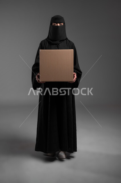 Illustrative panels and educational materials, marketing presentations and advertisements, a rectangular mock-up, a portrait of a veiled Saudi Arabian Gulf Muslim woman wearing a black abaya, standing straight and holding her hands, a blank beige canvas, full-length body, gray background