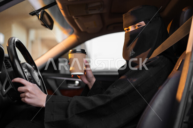 إحضار القهوة الساخنة في طريق العمل, حرية قيادة السيارة للمرأة السعودية، سيدة عربية خليجية سعودية مسلمة منقبة ترتدي العباءة التقليدية تجلس داخل سيارتها وتحمل بيدها كوب ورقي، مفهوم الحشمة والالتزام, اعتماد النساء على أنفسهن في وسائل النقل والمواصلات