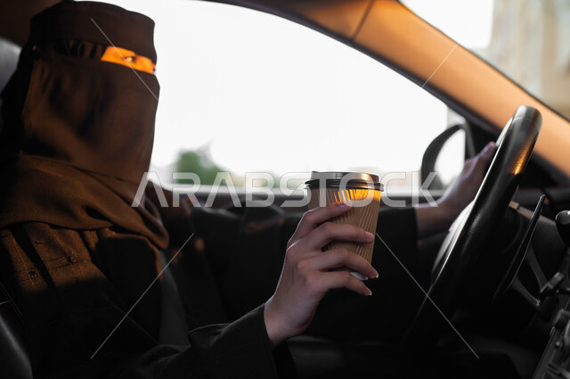 إحضار المشروب المفضل قبل الانطلاق, حرية قيادة السيارة للمرأة السعودية، سيدة عربية خليجية سعودية مسلمة منقبة ترتدي العباءة التقليدية تجلس داخل سيارتها وتمسك بيدها كوب ورقي، مفهوم الحشمة والالتزام, اعتماد النساء على أنفسهن في وسائل النقل والمواصلات