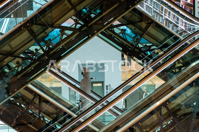 تأمين وسائل الراحة للقراء، مواطن عربي إماراتي خليجي يقف على السلم الكهربائي في مكتبة محمد بن راشد في امارة دبي، المكتبات العلمية في الامارات العربية المتحدة، التصاميم الداخلية الفاخرة، مكان للقراء ومحبي العلم والمعرفة، اكتساب المعرفة وتنمية الذخيرة اللغوية