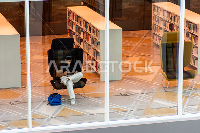 مكان للقراء ومحبي العلم والمعرفة، تأمين وسائل الراحة للقراء، اكتساب المعرفة وتنمية الذخيرة اللغوية، شاب عربي إماراتي خليجي يجلس على كرسي في مكتبة محمد بن راشد الثرية بالمجلات والمعاجم في امارة دبي، المكتبات العلمية في الامارات العربية المتحدة