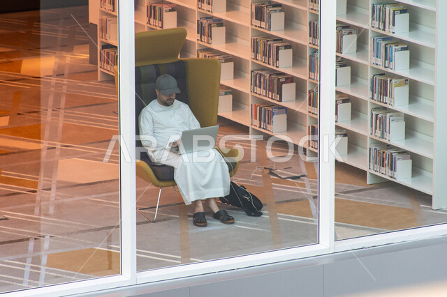 التنمية اللغوية واكتساب المعرفة، المكتبات العلمية في الامارات العربية المتحدة، مكان للقراء ومحبي العلم والمعرفة، تأمين وسائل الراحة للقراء، شاب عربي إماراتي خليجي يجلس على كرسي يعمل على حاسوبه الشخصي في مكتبة محمد بن راشد الثرية بالمجلات والمعاجم في امارة دبي