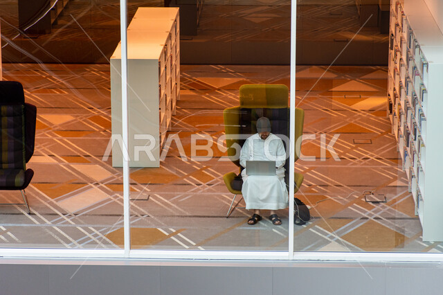 مكان للقراء ومحبي العلم والمعرفة، تأمين وسائل الراحة للقراء، اكتساب المعرفة والتنمية اللغوية، شاب عربي إماراتي خليجي يجلس على كرسي يعمل على حاسوبه الشخصي في مكتبة محمد بن راشد الثرية بالمجلات والمعاجم في امارة دبي، المكتبات العلمية في الامارات العربية المتحدة