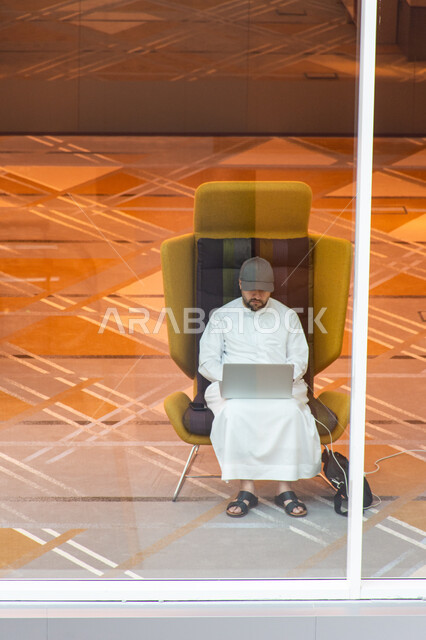 تأمين وسائل الراحة للقراء، مكان للقراء ومحبي العلم والمعرفة، اكتساب المعرفة والتنمية اللغوية، شاب عربي إماراتي خليجي يجلس على كرسي يعمل على حاسوبه الشخصي في مكتبة محمد بن راشد الثرية بالمجلات والمعاجم في امارة دبي، المكتبات العلمية في الامارات العربية المتحدة