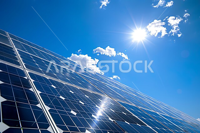 انعكاس اشعة الشمس على محطات الطاقات الشمسية المتجددة، مفهوم انتاج الطاقة البديلة الصديقة للبيئة في المملكة العربية السعودية, صورة مقربة لمجموعة من ألواح الطاقة الكهروضوئية، خلفية السماء الزرقاء مع الغيوم