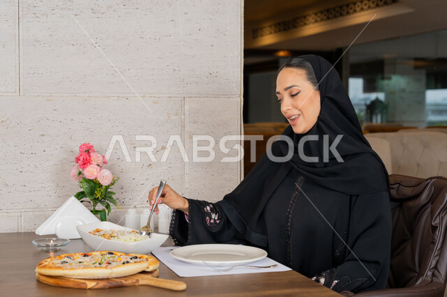 الاستمتاع بالأنشطة الترفيهية, قضاء الأوقات الممتعة في المطعم, امرأة عربية خليجية إماراتية محجبة ترتدي العباءة السوداء تجلس على المائدة و تقوم بتناول الطعام, تشكيلة متنوعة و مختلفة من المأكولات, مطاعم و كافيهات في الإمارات