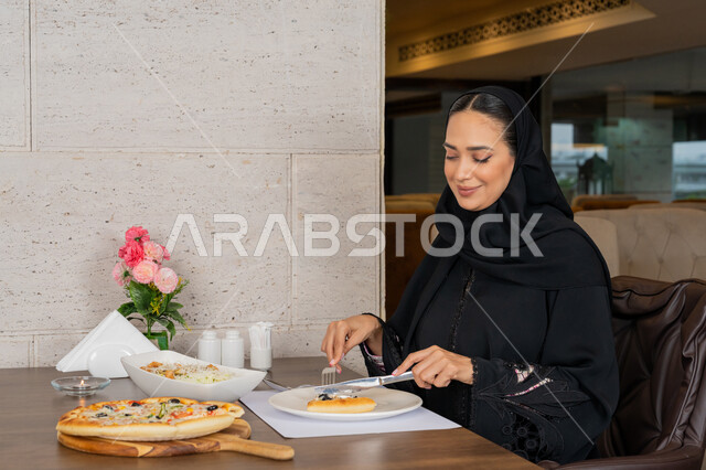 قضاء الأوقات الممتعة في المطعم, الاستمتاع بالأنشطة الترفيهية, امرأة عربية خليجية إماراتية محجبة ترتدي العباءة السوداء تجلس على المائدة و تقوم بتناول الطعام, تشكيلة متنوعة و مختلفة من المأكولات, مطاعم و كافيهات في الإمارات