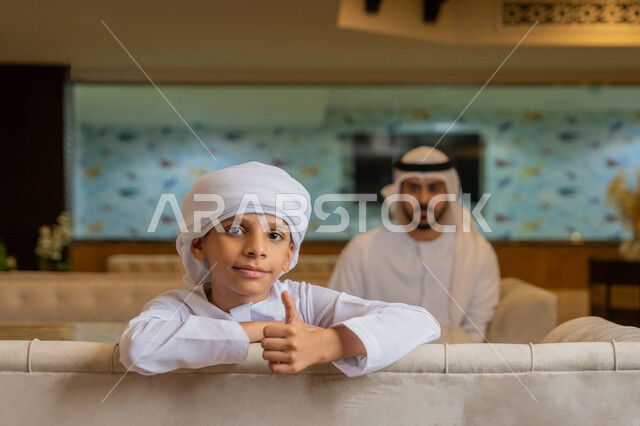 الإشارة بإصبع الإبهام للأعلى بتعابير الجودة, قضاء الأوقات الممتعة مع العائلة, رجل عربي خليجي إماراتي يرتدي الكندورة و الغترة البيضاء يجلس مع ابنه في أحد المطاعم, الأجواء الأسرية السعيدة, مشاركة الأبناء الأنشطة الترفيهية في الخارج