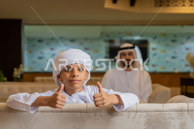الإشارة بإصبع الإبهام للأعلى بتعابير الجودة, قضاء الأوقات الممتعة مع العائلة, رجل عربي خليجي إماراتي يرتدي الكندورة و الغترة البيضاء يجلس مع ابنه في أحد المطاعم, الأجواء الأسرية السعيدة, مشاركة الأبناء الأنشطة الترفيهية في الخارج