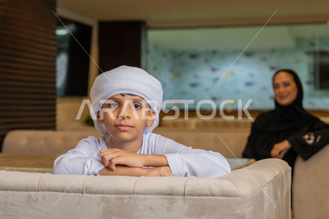النظر إلى الكاميرا بإيماءات السعادة و السرور, قضاء أوقات ممتعة في الخارج مع الأبناء, أم و ابن عربيان خليجيان إماراتيان يرتديان الثوب التقليدي الإماراتي يجلسان في أحد المطاعم, أجواء عائلية سعيدة, مفهوم الترابط الأسري