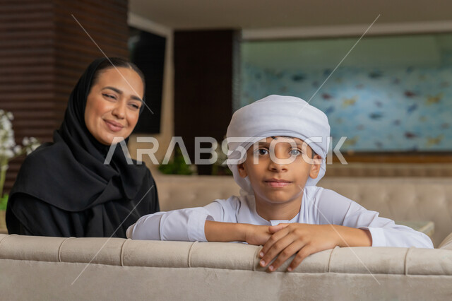 قضاء الأوقات الممتعة مع الأبناء, مفهوم الألفة و المحبة بين أفراد الأسرة, أجواء عائلية سعيدة مليئة بالحنان, امرأة عربية خليجية إماراتية محجبة ترتدي العباءة السوداء تجلس بجانب ابنها في المطعم و تنظر إليه بتعابير الحب و المودة