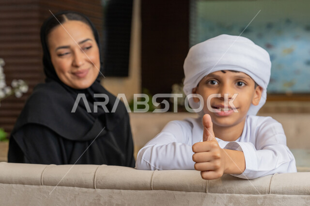 الإشارة بإصبع الإبهام للأعلى بتعابير الجودة, مفهوم الألفة و المحبة بين أفراد الأسرة, امرأة عربية خليجية إماراتية محجبة ترتدي العباءة السوداء تجلس بجانب ابنها في المطعم و تنظر إليه بتعابير الحب و المودة, قضاء الأوقات الممتعة مع الأبناء