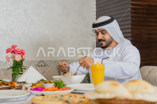 الاستمتاع بتناول الأطباق الشهية, تشكيلة متنوعة و مختلفة من المأكولات والمشروبات, رجل عربي خليجي إماراتي يرتدي الكندورة و الغترة البيضاء يجلس على المائدة يقوم بتناول الغداء, مطاعم و كافيهات في الإمارات, قضاء الأوقات الممتعة في المطعم