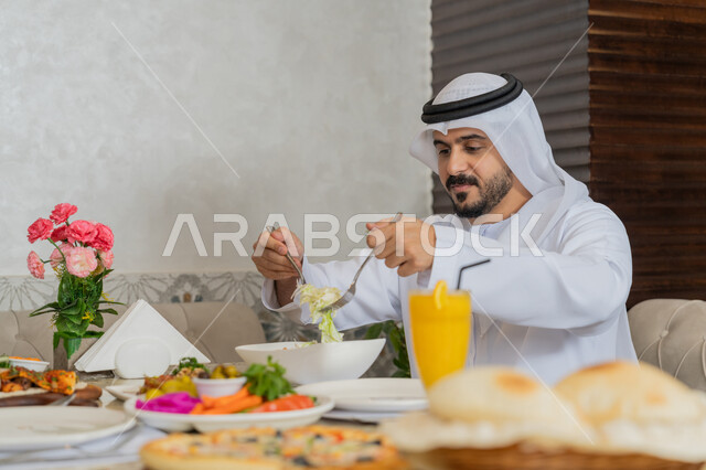 تشكيلة متنوعة و مختلفة من المأكولات والمشروبات, الاستمتاع بتناول الأطباق الشهية, رجل عربي خليجي إماراتي يرتدي الكندورة و الغترة البيضاء يجلس على المائدة يقوم بتناول الغداء, مطاعم و كافيهات في الإمارات, قضاء الأوقات الممتعة في المطعم