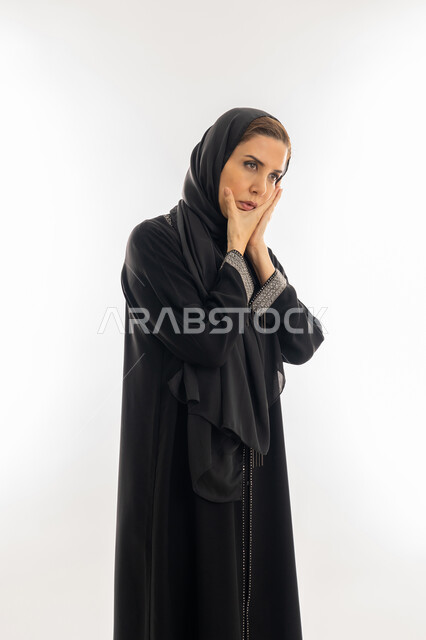 الشعور بألم الأسنان وتسوس الأضراس, سيدة سعودية بحاجه لزيارة طبيب الأسنان، بورتريه لإمراة عربية إماراتية خليجية ترتدي العباءة والحجاب تضع يدها على خدها، إيماءات وجه ويدين تدل على الالم ووجع الفم، خلفية بيضاء