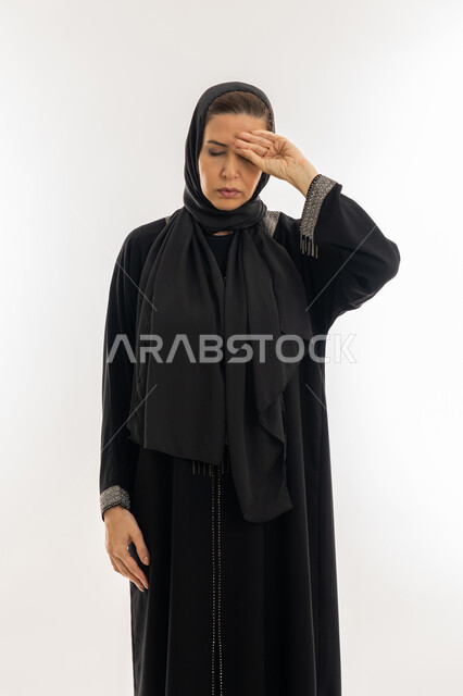 الإرهاق و التعب و الحاجه للعلاج, طلب المساعده للذهاب الى المستشفى، بورتريه مقرب لسيدة عربية سعودية محجبة ترتدي العباءة السوداء تضع يدها على رأسها بتعابير الدوخة وعدم التوازن, امرأة خليجية اماراتية تشعر بالمرض و الصداع, خلفية بيضاء