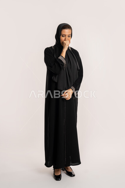 الكحة والتهاب الحلق والحاجة للعلاج، الإصابة بالأنفلونزا ونزلات البرد, إيماءات الإرهاق والتعب الشديد، بورتريه لإمرأة مسنة عربية خليجية اماراتية ترتدي الحجاب والعباءة تضع يدها أمام فمها وتقوم بالسعال, خلفية بيضاء