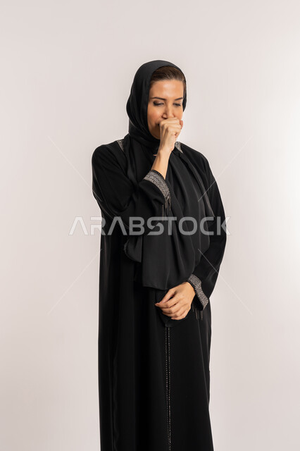الكحة والتهاب الحلق والحاجة للعلاج، الإصابة بالأنفلونزا ونزلات البرد, إيماءات الإرهاق والتعب الشديد، بورتريه لإمرأة مسنة عربية خليجية اماراتية ترتدي الحجاب والعباءة تضع يدها أمام فمها وتقوم بالسعال, صورة الجسم بالكامل، خلفية بيضاء