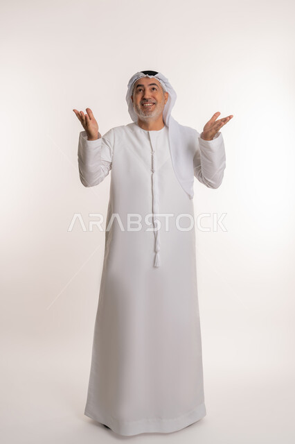 Pointing to something, gestures indicating reception and welcome, gestures of happiness and joy when seeing someone, portrait of an elderly Arab Emirati Gulf man wearing a kandura and ghutra raising his arms up with expressions of joy, full body image, white background