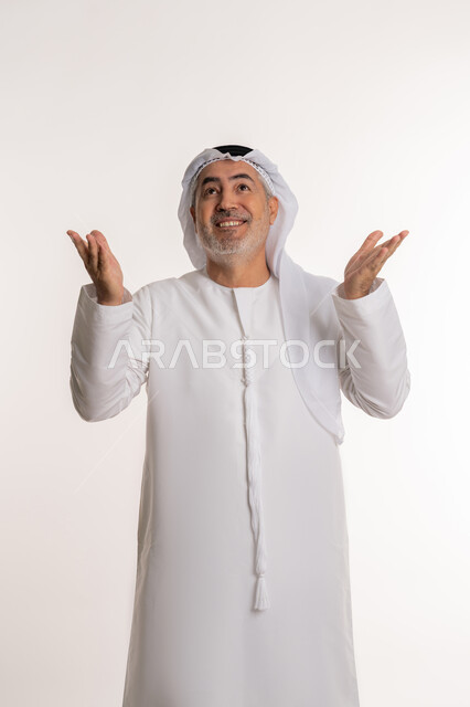 حركات تدل على الاستقبال و الترحيب، ايماءات السعادة والفرح عند رؤية شخص ما, الاشارة الى شيء ما, بورتريه لرجل مسن عربي اماراتي خليجي يرتدي الكندورة و الغترة يرفع ذراعيه للاعلى بتعابير الفرح, خلفية بيضاء