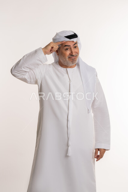 تعابير الوجه ولغة الجسد المختلفة, بورتريه لرجل كبير بالسن عربي اماراتي خليجي يرتدي الكندورة الاماراتية والغترة يرفع اليد اليسرى لإلقاء التحية, ايماءات تدل على السعادة, مفهوم السلام والترحيب, خلفية بيضاء