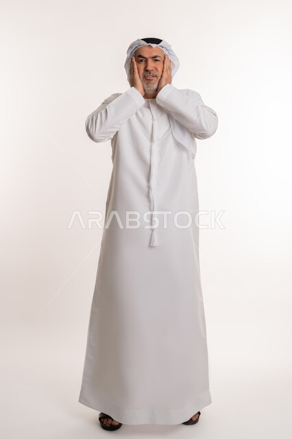 الإحساس بوجع الرأس و الدوخة, الحاجة للعلاج والراحة، آلام الشقيقة والصداع النصفي ,إيماءات الألم والتعب والمرض, بورتريه لرجل كبير السن عربي خليجي اماراتي يرتدي الغترة والكندورة يضع يديه على رأسه يشعر بالدوار, صورة الجسم بالكامل، خلفية بيضاء