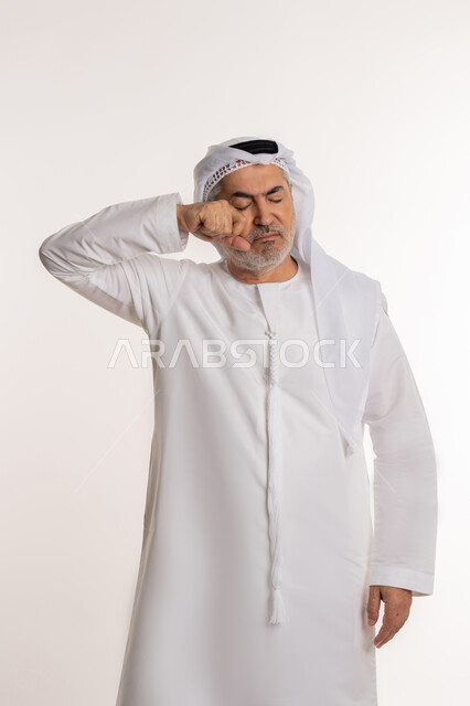 الخسارة والفشل والندم على شيء ما، بورتريه لرجل كبير بالسن عربي خليجي إماراتي يرتدي الغترة والكندورة التقليدية يإيماءات وجه ويدين تدل على الشعور بالحزن والإحباط والرغبة بالبكاء، خلفية بيضاء