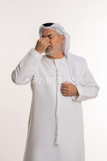 وضع اليد على الوجه والضفط على العيون من شدة الوجع, تذكر شيء محدد بشكل مفاجئ, بورتريه لرجل كبير بالسن عربي خليجي اماراتي يرتدي الكندورة التقليدية والغترة يعاني من مشاكل في النظر بسبب تقدم العمر, خلفية بيضاء