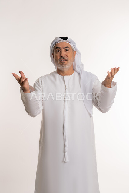 التساؤل والإستغراب والاستفسار عن أمر ما، الغموض وعدم الوضوح، الإستفهام حول موضوع معين, بورتريه لرجل كبير بالسن عربي خليجي اماراتي يرتدي الكندورة والغترة يرفع يديه نحو الأعلى بإيماءات عدم المعرفة, خلفية بيضاء