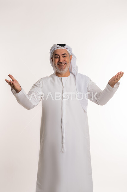 حركات تدل على الاستقبال و الترحيب، ايماءات السعادة والفرح عند رؤية شخص ما, الاشارة الى شيء ما, بورتريه لرجل مسن عربي اماراتي خليجي يرتدي الكندورة و الغترة يرفع ذراعيه للاعلى بتعابير الفرح, خلفية بيضاء