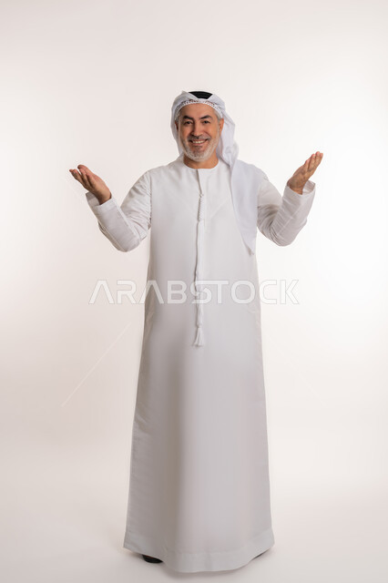 ايماءات السعادة والفرح عند رؤية شخص ما, حركات تدل على الاستقبال و الترحيب, الاشارة الى شيء ما, بورتريه لرجل مسن عربي اماراتي خليجي يرتدي الكندورة و الغترة يرفع ذراعيه للاعلى بتعابير الفرح, صورة الجسم بالطول الكامل, خلفية بيضاء