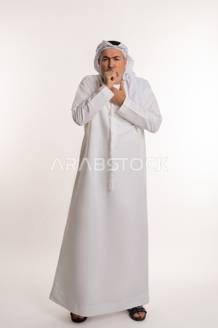 الكحة والتهاب الحلق والحاجة للعلاج، الإصابة بالأنفلونزا ونزلات البرد, إيماءات الإرهاق والتعب الشديد، بورتريه لرجل كبير بالسن عربي خليجي اماراتي يرتدي الكندورة والغترة يضع يده أمام فمه ويقوم بالسعال, صورة الجسم بالكامل، خلفية بيضاء