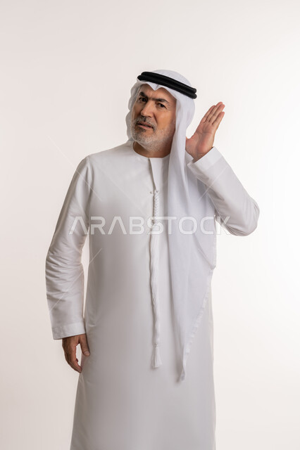 ضعف السمع عند الكبار بالعمر والمسنين، التنصت والتجسس خلسة، الاستماع الى الاسرار والمحادثات, بورتريه لرجل كبير بالسن عربي إماراتي خليجي يضع يده خلف أذنه بايماءات تدل على الانصات، التركيز في الكلام، خلفيه بيضاء
