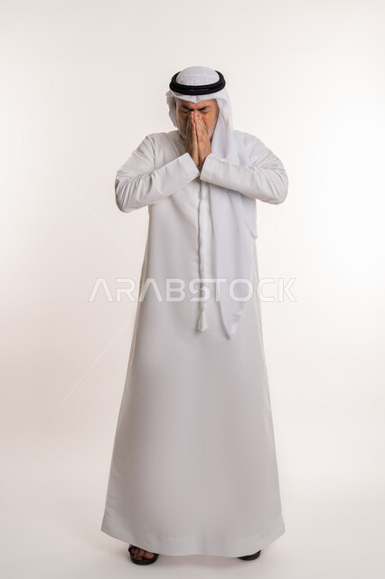 الشعور بالمرض و الزكام والحاجة الى العلاج والدواء, التهاب الأنف التحسسية, بورتريه من الجانب لرجل كبير بالسن عربي اماراتي خليجي يرتدي الغترة والكندورة يضع يديه على وجهه بإيماءات العطاس, صورة الجسم بالطول الكامل, خلفية بيضاء