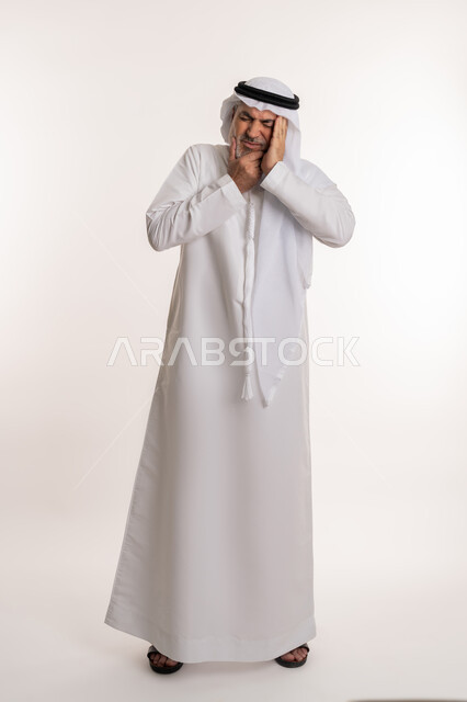 Gingivitis and tooth decay, request for treatment and help, portrait of an elderly Arab Gulf Emirati man wearing a kandura and ghutra, putting his hand on his cheek with gestures indicating feeling toothache, need to visit a doctor, full body, white background