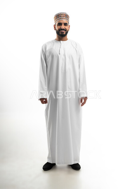 The concept of personal hygiene, concern for one's appearance, elegance in wearing traditional clothes, portrait of an Omani Arab young man wearing a dishdasha and a kummah looking at the camera with a smiling expression, white background