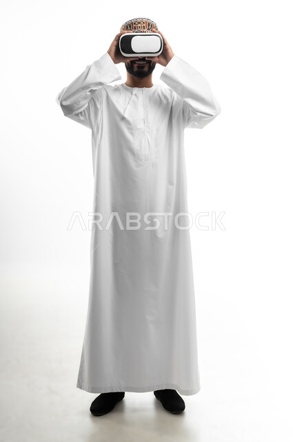 بورتريه لشاب عربي خليجي عماني يرتدي نظارات ثلاثية الأبعاد، مفهوم الاندماج ومحاكاة العالم الخيالي، المتعة و التسلية بالمشاهدة عبر نظارة الواقع الافتراضي، ايماءات وجه تدل على الفرح والسرور, خلفية بيضاء