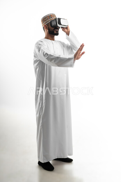 الاندماج ومحاكاة العالم الخيالي، المتعة و التسلية بالمشاهدة عبر نظارة الواقع الافتراضي, بورتريه لشاب عربي خليجي عماني يرتدي نظارات ثلاثية الأبعاد, محاولة رفع اليد دليل على التفاعل, خلفية بيضاء