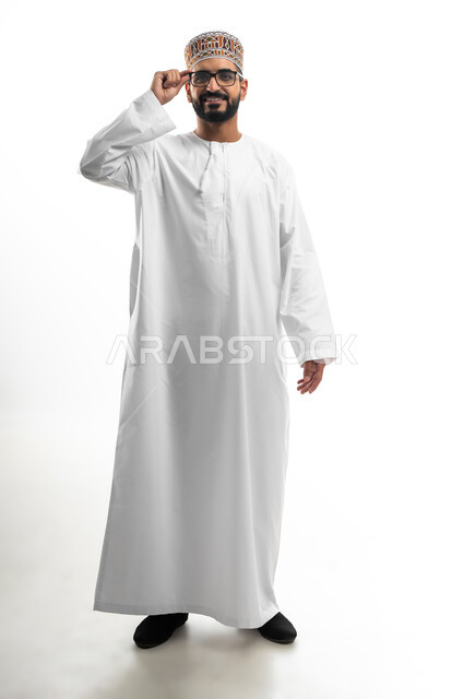 الرؤية من خلال العدسات الطبية, إيماءات السعادة و السرور بوضوح الصورة, بورتريه لشاب عربي خليجي عماني يرتدي النظارة الخاصة بضعف النظر ،مفهوم تحسين الرؤية و محاولة تعديل البصر, صورة الجسم بالطول الكامل, خلفية بيضاء