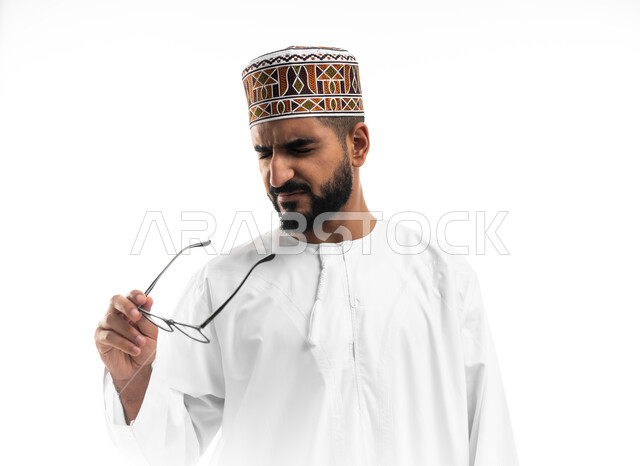 استخدام البصريات لتوضيح الرؤية، بورتريه لرجل عربي خليجي عماني يرتدي الزي العماني التقليدي تظهر عليه علامات الانزعاج, العدسات الخاصة بضعف النظر ، الإبصار من خلال النظارة الطبية ، مفهوم الضبابية وعدم وضوح الرؤية  ، خلفية بيضاء